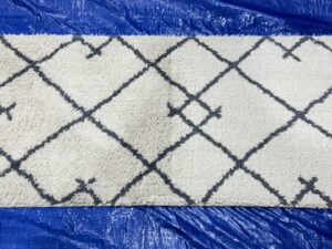 A white and grey patterned area rug laid on a blue tarp, undergoing professional cleaning by Strictly Tile & Carpet Care in Lansing, MI.
