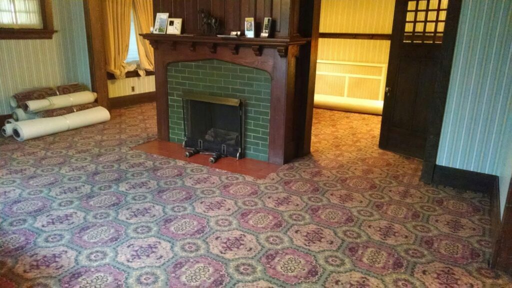 A room with patterned carpet, showing rolls of carpet in the background, indicating an installation by Home Based Carpet & Flooring in Cincinnati, OH.