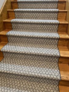A patterned carpet runner expertly installed on a wooden staircase by Harry's Carpet One in Quincy, MA.