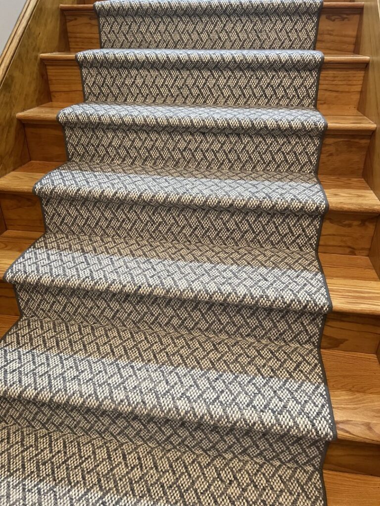 A patterned carpet runner expertly installed on a wooden staircase by Harry's Carpet One in Quincy, MA.
