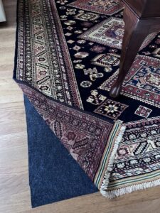 A patterned rug partially lifted to show a rug pad underneath on a hardwood floor by Rug Masters in Charleston, SC.