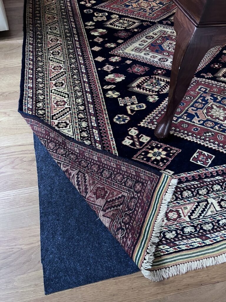 A patterned rug partially lifted to show a rug pad underneath on a hardwood floor by Rug Masters in Charleston, SC.