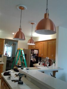 Electrician installing modern pendant lights in a kitchen, with tools on the counter, by In the Light Electrical LLC in Kansas City, KS
