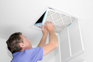 A person changing an air filter in a ceiling HVAC vent, a common maintenance service by Custom Heating & Air Conditioning - Nampa in Nampa, ID.