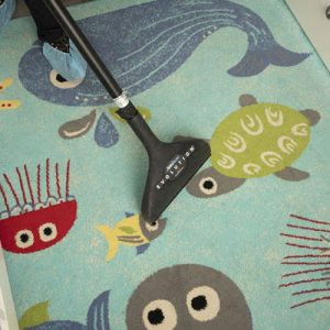 A professional cleaning a colorful kids' area rug with a carpet cleaning wand at Cosmo Carpet Cleaning in Princeton, NJ.