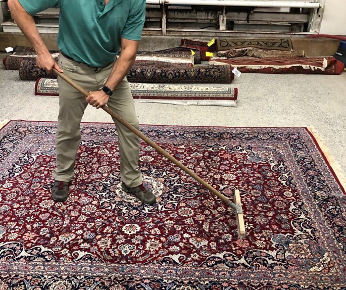 A person cleaning a large oriental rug with a grooming tool at Rug Masters in Charleston, SC.