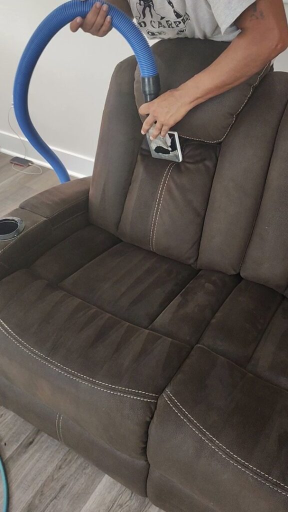 A person cleaning an upholstered recliner with professional equipment by D&D Carpet Cleaning & Janitorial in West Columbia, SC