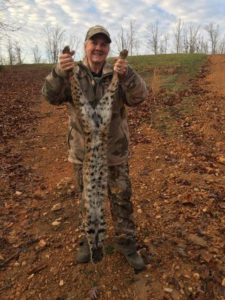 A person in camouflage holding a captured bobcat, showcasing wildlife removal services by ACB Wildlife Control in Memphis, TN.