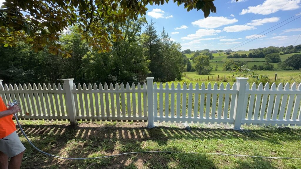 A person painting a white picket fence with a spray gun, a service by Pileggi Fence Painting in Franklin, TN