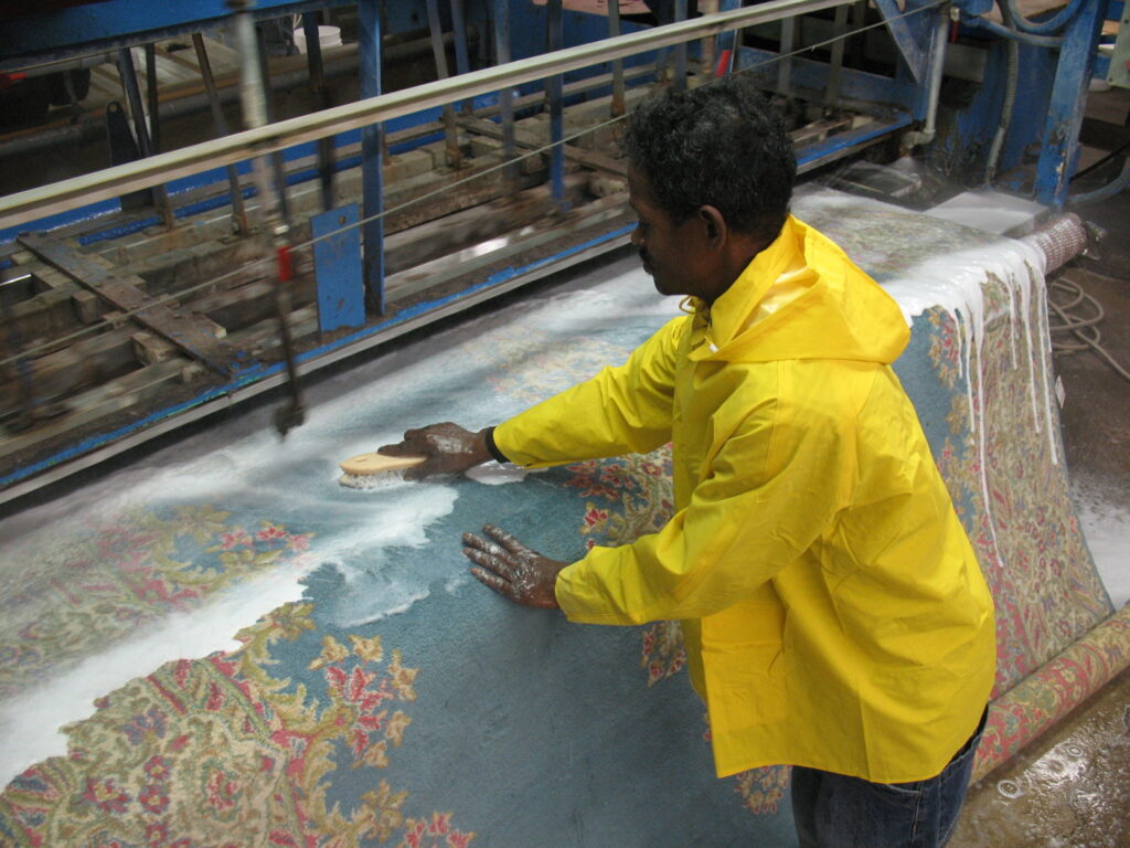 A professional technician scrubbing a large oriental rug on a specialized cleaning machine at Zakian Rug Cleaning in Philadelphia, PA