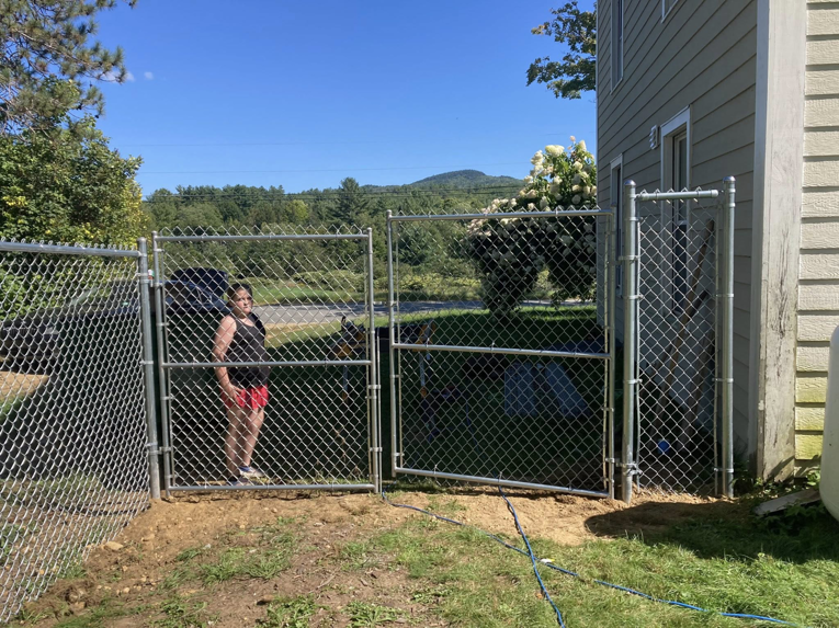 A person standing inside a newly installed chain-link fence with double gates by Profence in Leander, TX.
