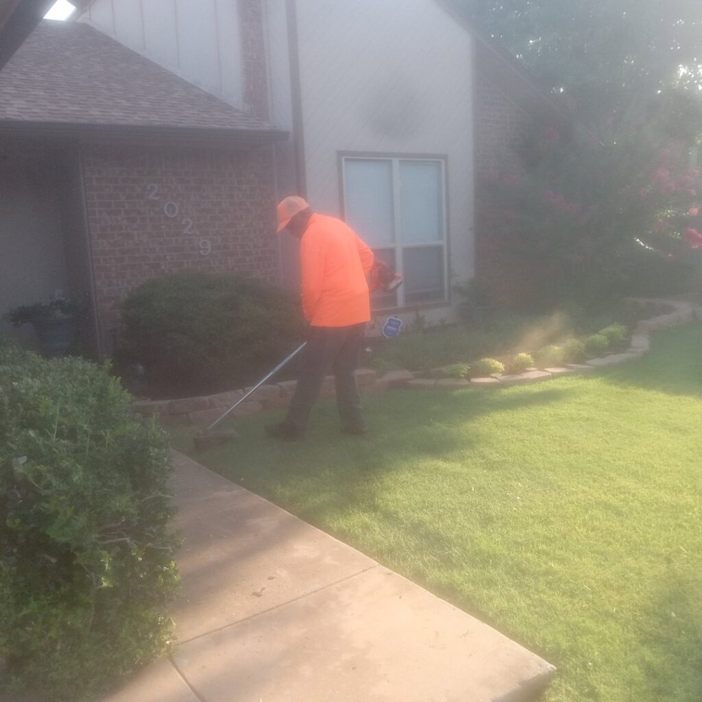 A person using a string trimmer to edge a lawn along a sidewalk for A & A Lawn Care Service LLC in Edmond, OK.
