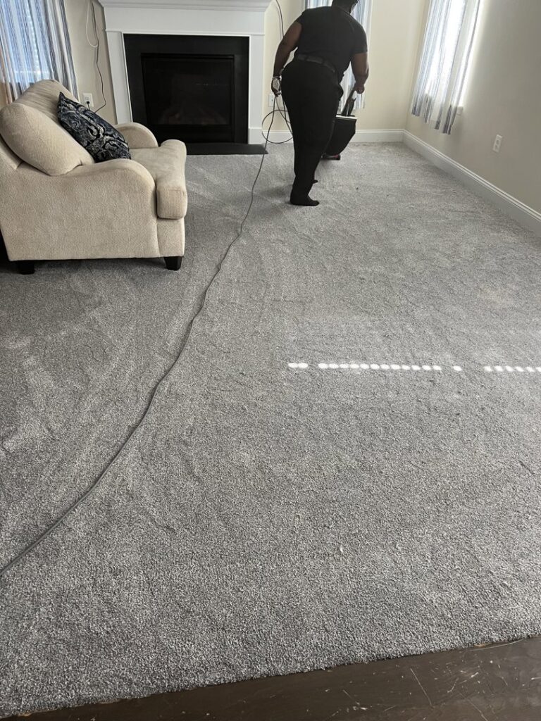 A person vacuuming a newly installed grey carpet in a living room by Danny's Flooring Service LLC in White Plains, MD