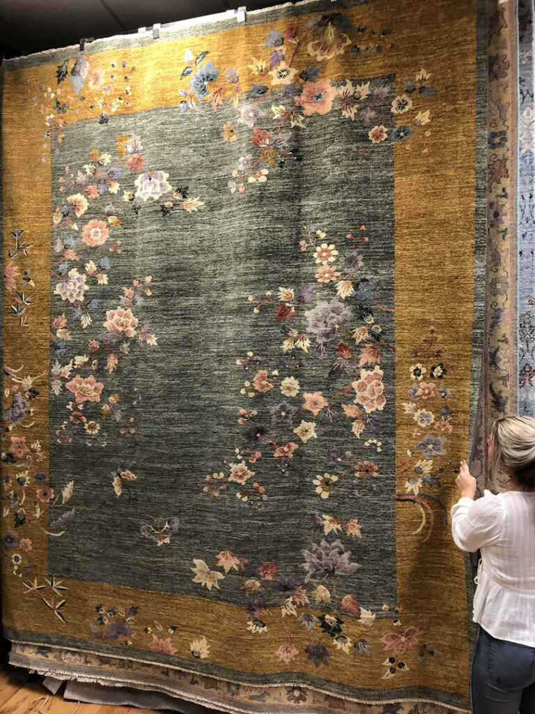A person viewing a large, ornate oriental rug hanging in the showroom at Rug Masters in Charleston, SC.