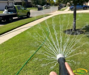 A person watering a residential lawn with a hose, with a C-Green Lawns truck in the background in Yukon, OK.