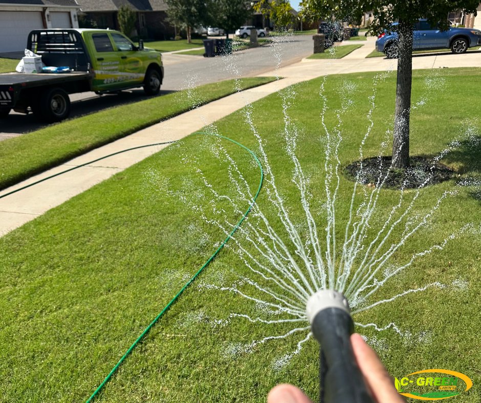 A person watering a residential lawn with a hose, with a C-Green Lawns truck in the background in Yukon, OK.
