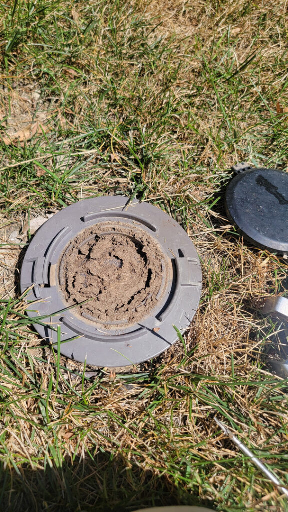 A pest bait station installed in the ground, used by KC Pest Experts for pest control services in Olathe, KS.