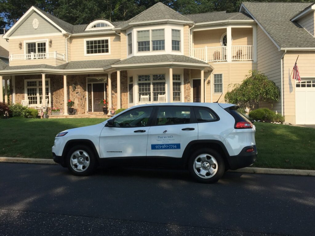 A white Pest by MD service vehicle parked in front of a residential home in Jersey City, NJ.