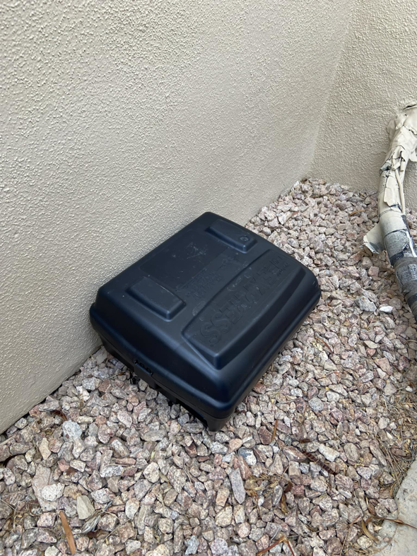 A black pest control bait station placed on gravel by Aloe Pest Control in Mesa, AZ.