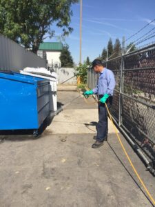A Dan's Pest Management technician spraying around a dumpster area for pest control in Bakersfield, CA