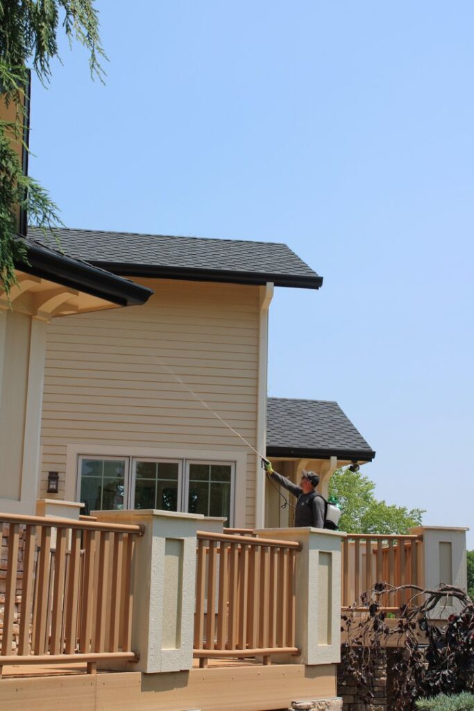 An Upfront Pest technician treating house eaves from a deck for pest control in North Kansas City, MO.