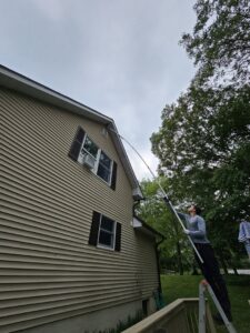 A pest control technician treating the eaves of a house with a long pole sprayer for Serene Property Services LLC in Albany, NY