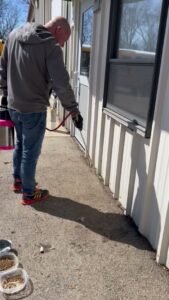 A pest control expert spraying along the foundation of a commercial building for Modern Solutions Pest Control in Rockford, IL.