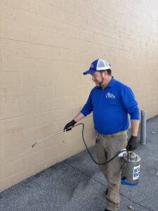 A Blue Beetle Pest Control expert spraying the foundation of a building for pest prevention in Kansas City, MO.