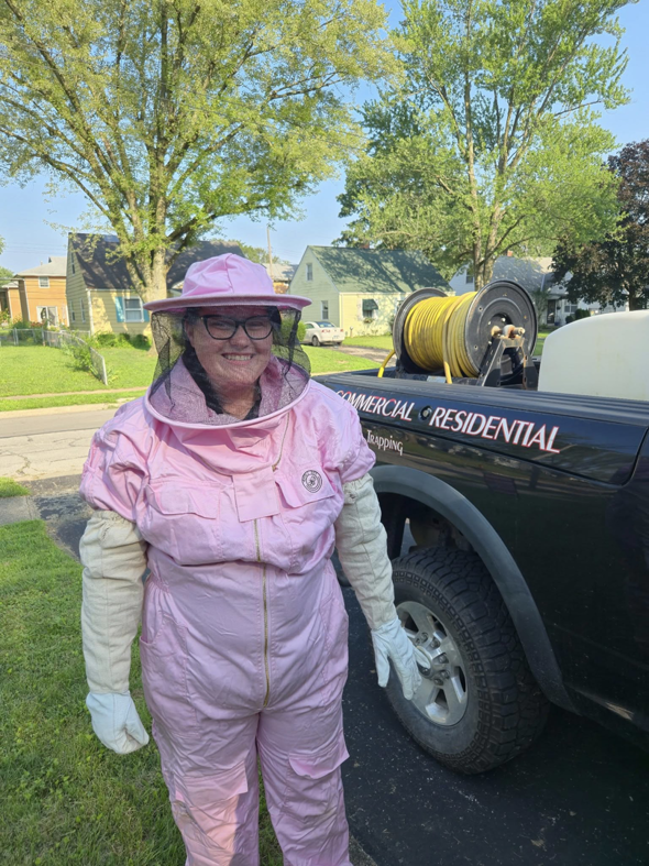 A pest control professional in a pink beekeeper suit standing next to a Stryker Pest Control LLC truck in Columbus, OH.