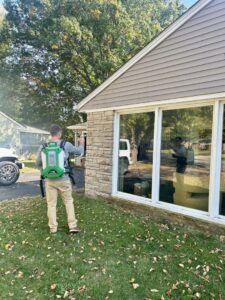 A pest control specialist using a backpack sprayer to treat the exterior of a residential house for Modern Solutions Pest Control in Rockford, IL.