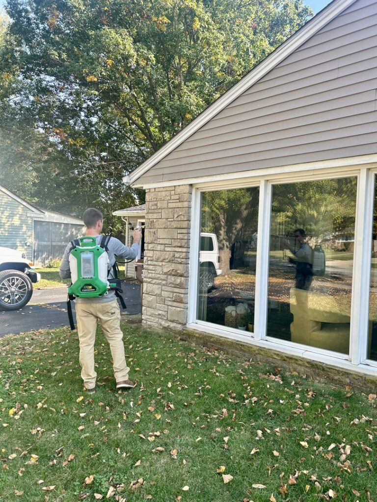A pest control specialist using a backpack sprayer to treat the exterior of a residential house for Modern Solutions Pest Control in Rockford, IL.