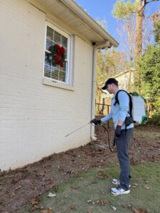A pest control specialist from Quest Pest Control spraying the exterior foundation of a house in Birmingham, AL.