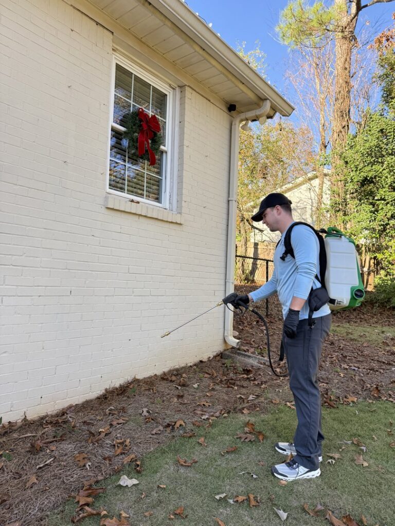 A pest control specialist from Quest Pest Control spraying the exterior foundation of a house in Birmingham, AL.