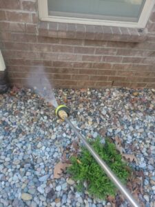 A pest control technician from A Plus Pest Control spraying the ground near a house foundation in Huntsville, AL.