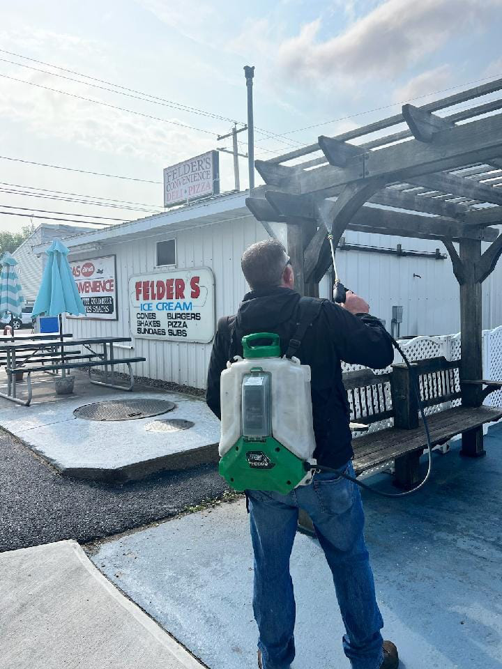 A pest control technician spraying a wooden pergola at a commercial property for Professional Pest Control Services in Rush, NY.