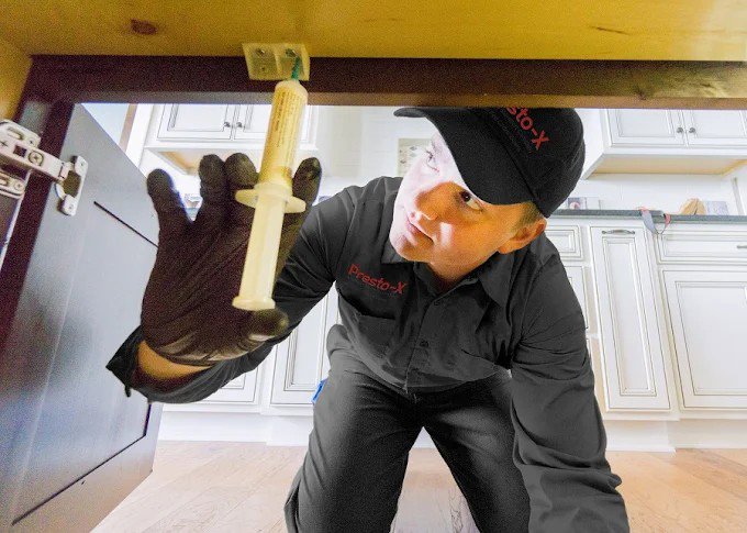 A pest control technician applying pest control bait under a kitchen cabinet for X-Out Pests Control in Little Rock, AR.
