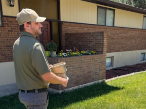 A pest control technician from Gravity Pest Control applying granules around a residential home in Caldwell, ID.