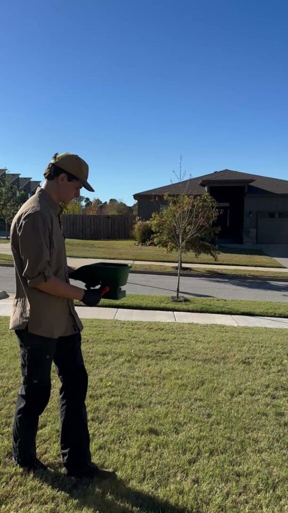 A pest control technician applying granules to a residential lawn for Ozark Pest Control in Fayetteville, AR.