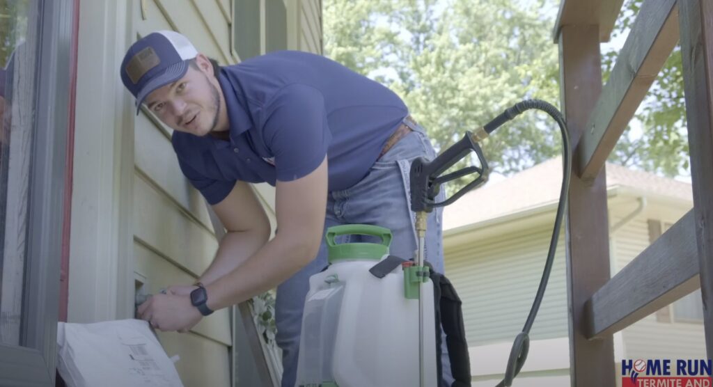 A pest control technician from Home Run Termite and Pest Services applying treatment to a home's exterior in Mayetta, KS.