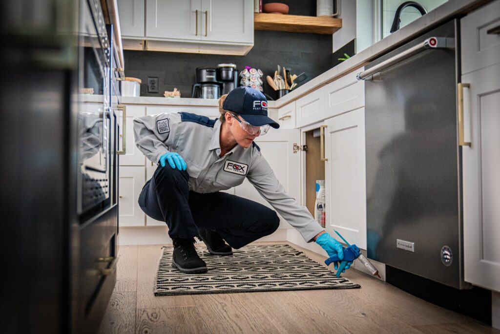 A Fox Pest Control technician applying pest treatment under a kitchen cabinet in Glen Ellyn, IL