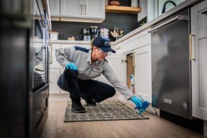 A Fox Pest Control technician applying pest treatment under a kitchen cabinet in Glen Ellyn, IL