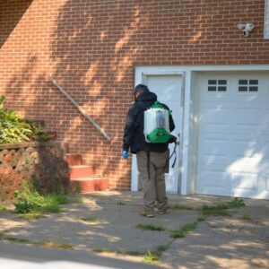A pest control technician with a backpack sprayer walking towards a residential house for 1st Choice Pest Solutions in Eau Claire, WI.
