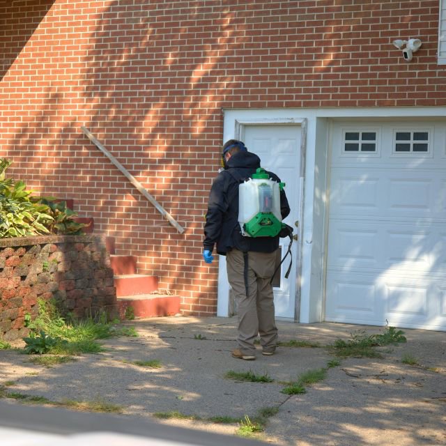 A pest control technician with a backpack sprayer walking towards a residential house for 1st Choice Pest Solutions in Eau Claire, WI.