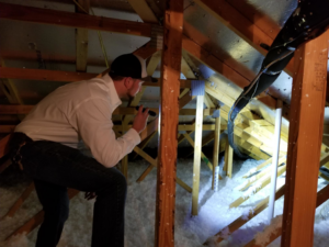 A GPM - Gruene Pest Management technician inspecting an attic with a flashlight for pests in San Antonio, TX.