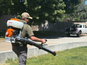 A pest control technician from Gravity Pest Control using a backpack sprayer to treat a lawn in Caldwell, ID.