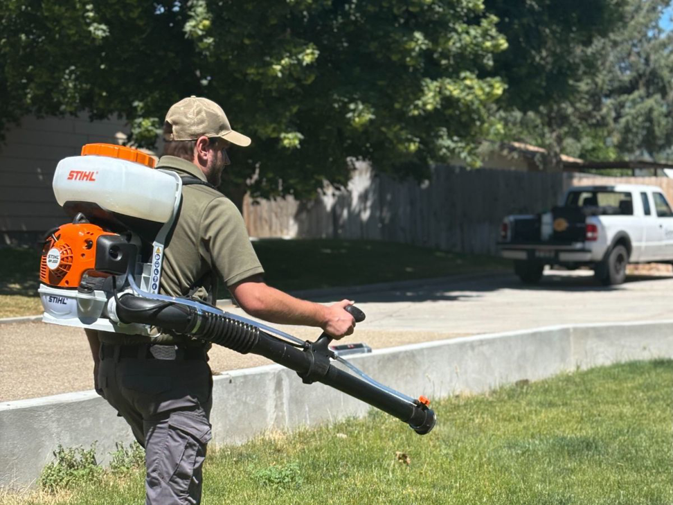 A pest control technician from Gravity Pest Control using a backpack sprayer to treat a lawn in Caldwell, ID.