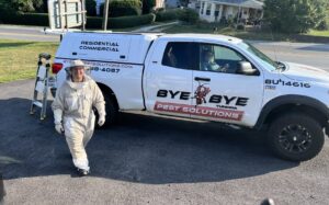 A Bye Bye Pest Solutions technician in a protective bee suit next to a company truck in Hanover, PA.