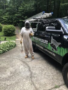 A Southern Pest Mgmt technician in a full bee suit with a shovel and spray can next to a company truck in Johns Creek, GA, ready for pest control.