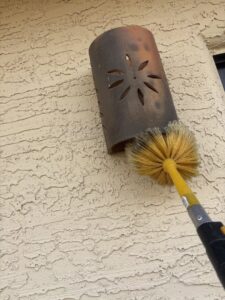 A pest control technician from Sandstorm Pest Control brushing a vent on the side of a house in Chandler, AZ.