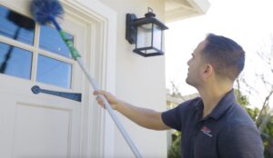 A pest control technician from Z Best Pest Solutions cleaning cobwebs or nests from a door frame in San Jose, CA.